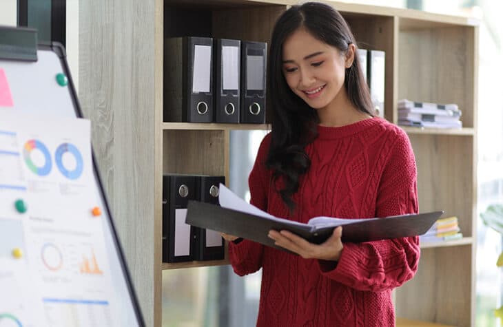 an asian woman happily looking over documents.